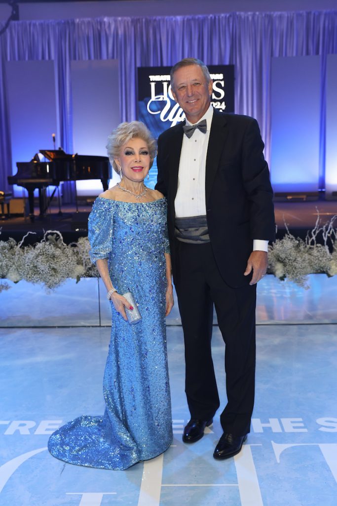 An older couple poses at the Lights Up Gala; the woman wears a blue sequined gown, and the man wears a tuxedo.