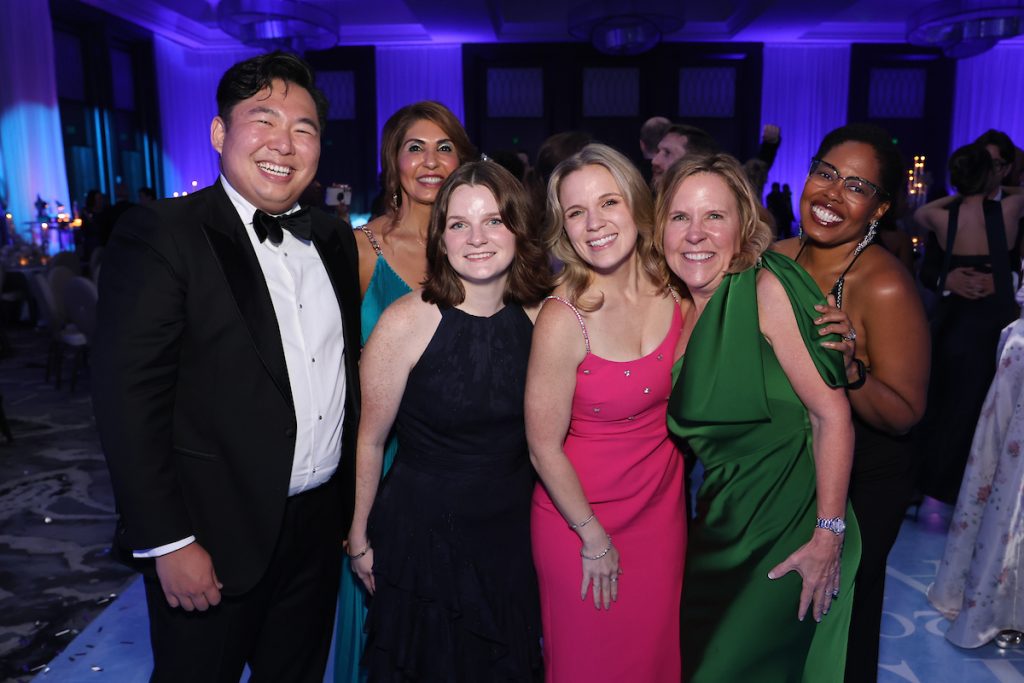 A group of six guests in colorful dresses and tuxedos pose together at the gala.